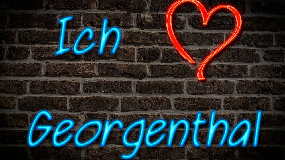 Eine Ziegelwand mit Neonreklamen, die "Ich Georgenthal" schreiben und ein Herzsymbol zeigt.