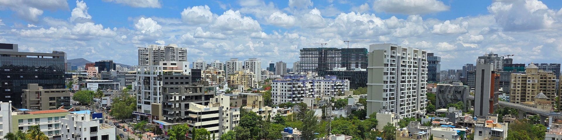 A cityscape with various buildings, including high-rises and mid-rise structures, under a partly cloudy sky.