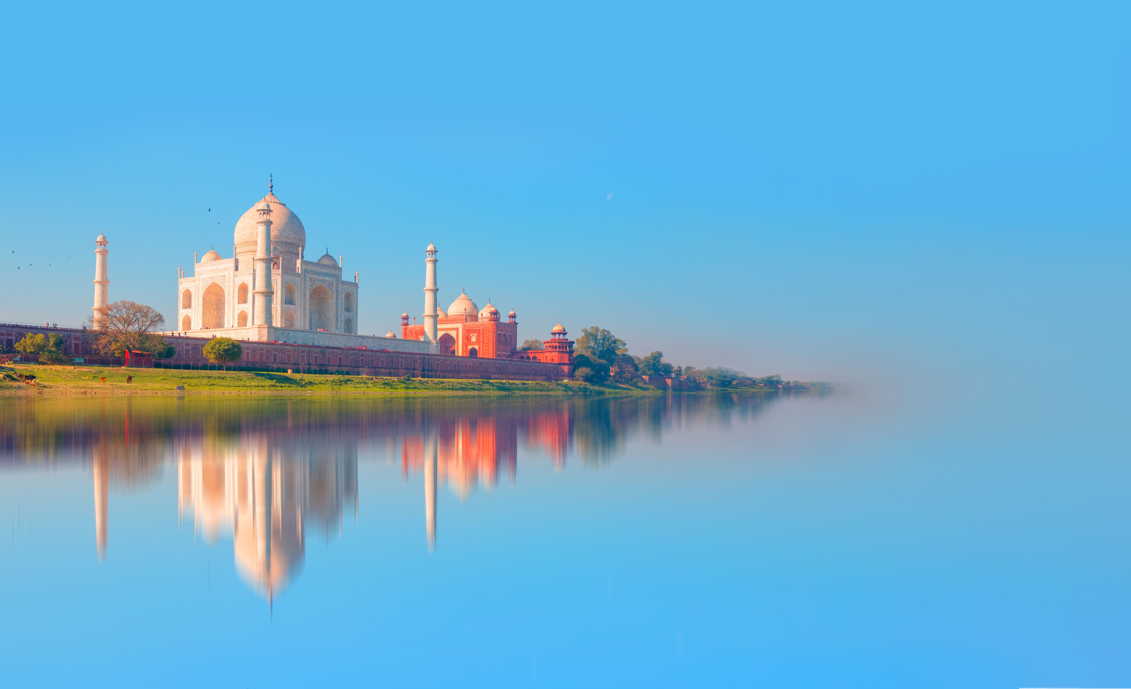 El Taj Mahal con su reflejo en el agua, un cielo despejado y un lago tranquilo.