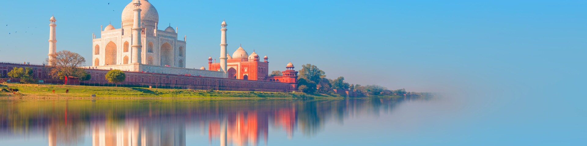 El Taj Mahal con su reflejo en el agua, un cielo despejado y un lago tranquilo.