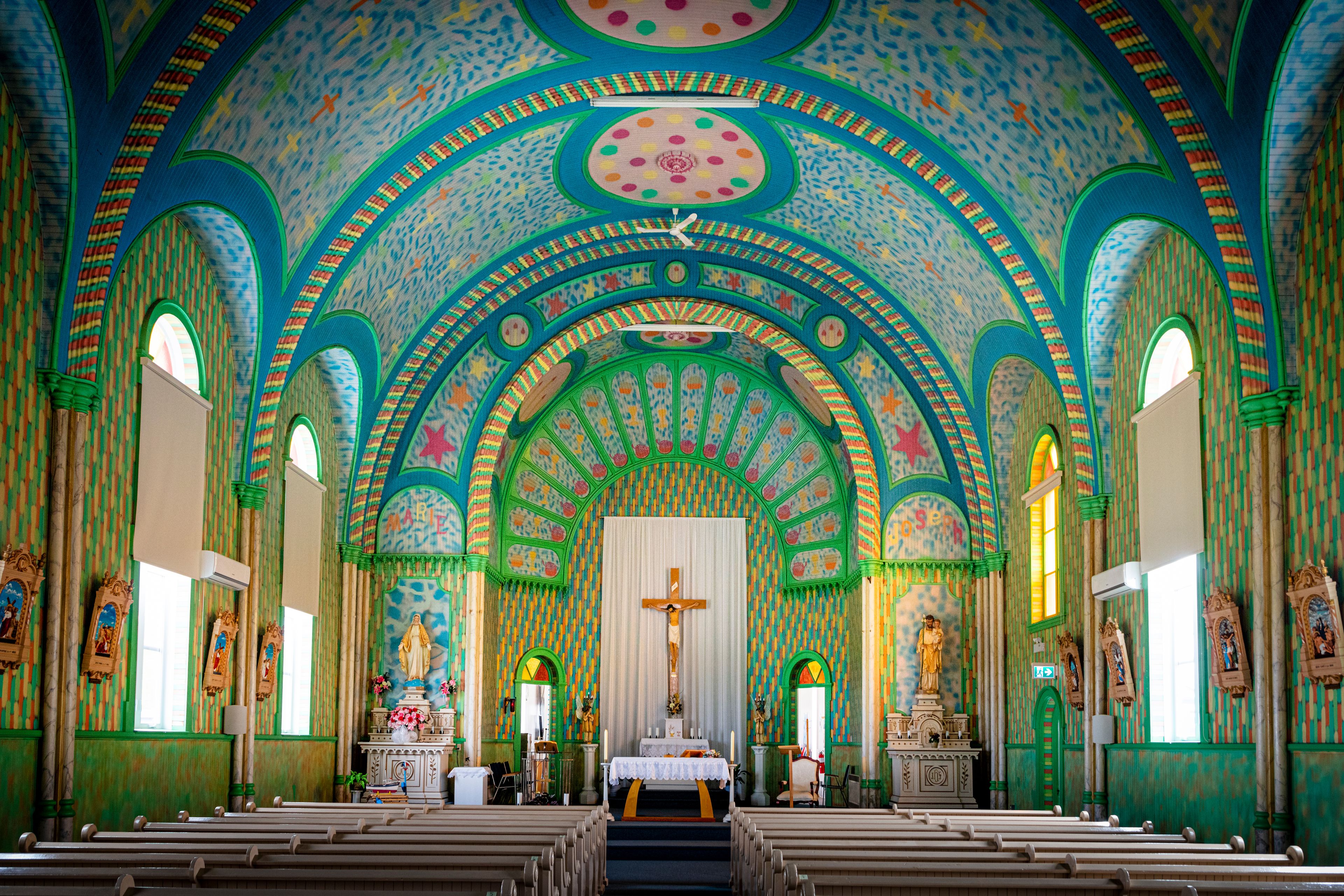 An ornate church interior with colorful mosaics, arched ceilings, and religious statues.