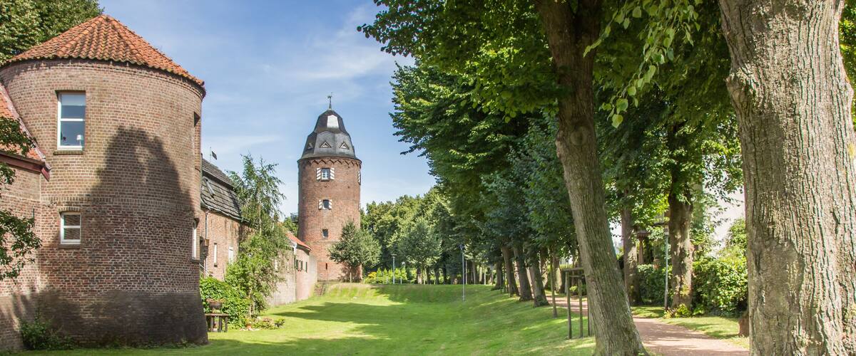A brick building with a tower and a pathway lined with trees.