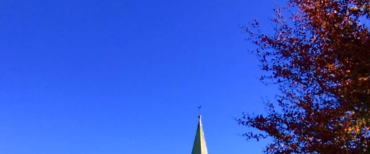 A church with a tall steeple and a graveyard in front.