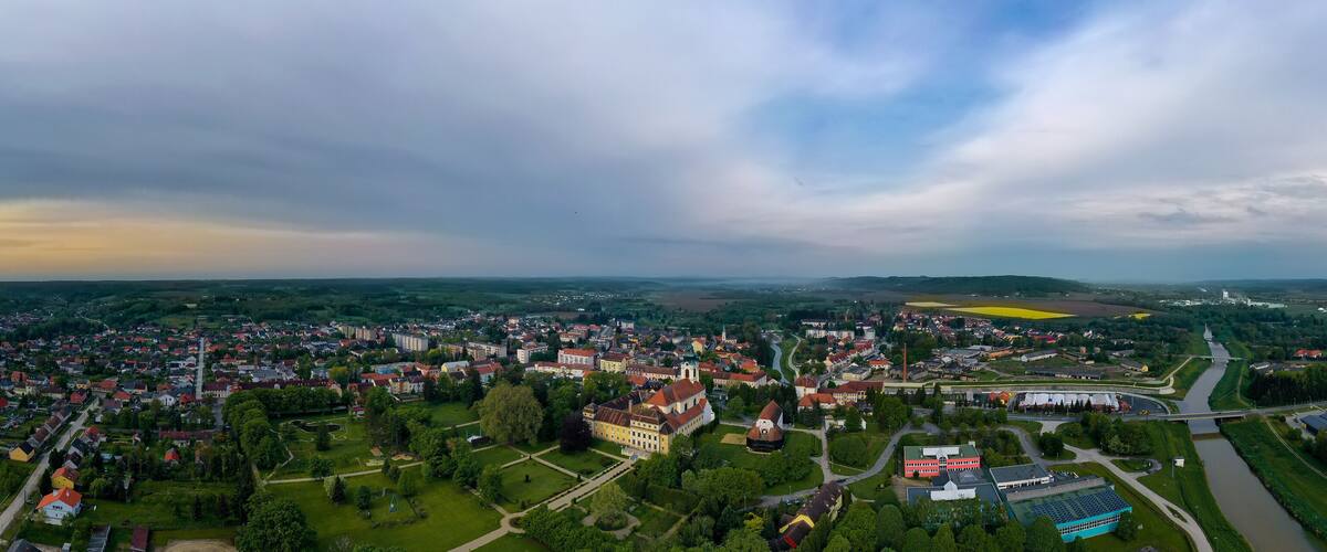 An aerial view of a town with a river, green fields, and a large building with a red roof.