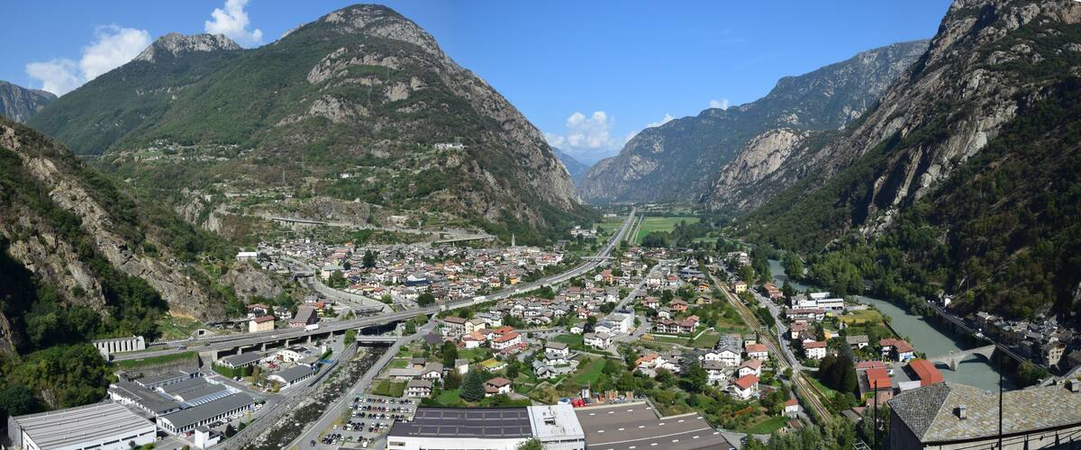 A valley with a river, a bridge, and a town surrounded by mountains.