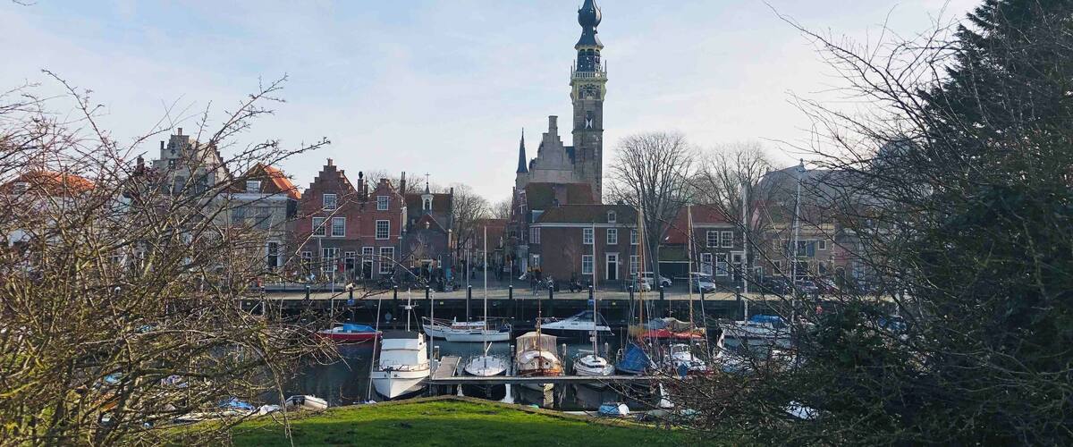 A town with a prominent clock tower, a marina with boats, and surrounding buildings.