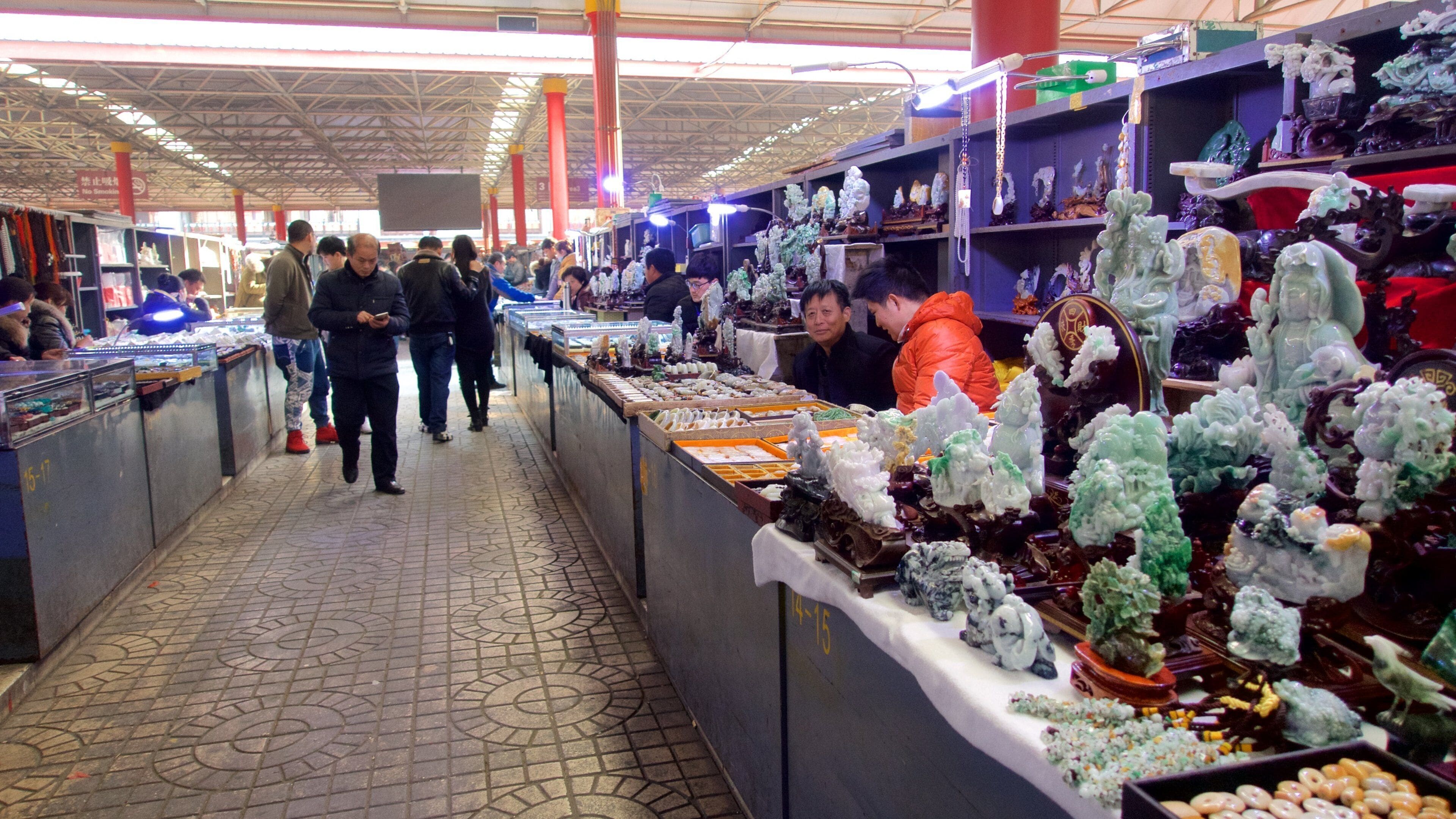 A bustling market with various stalls selling items like jade and ceramics.