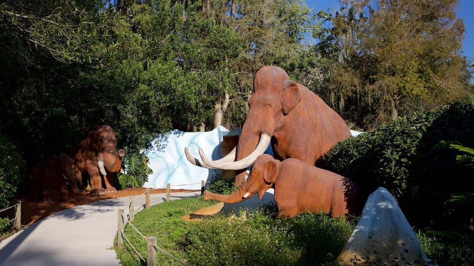 A large bronze elephant sculpture in a natural setting with trees and a paved path.
