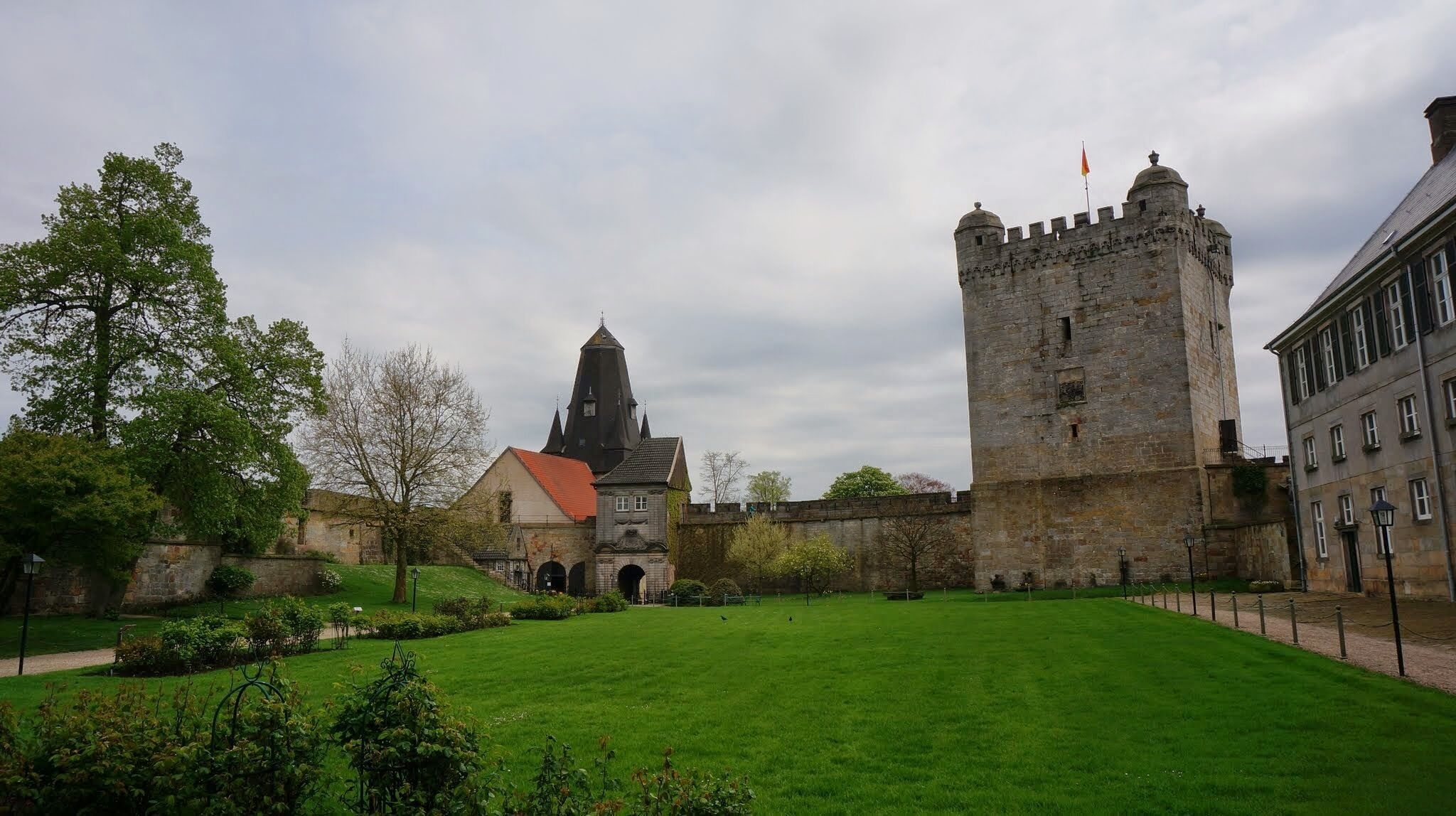 A historic castle with a tower, a church with a pointed roof, and a well-maintained lawn.