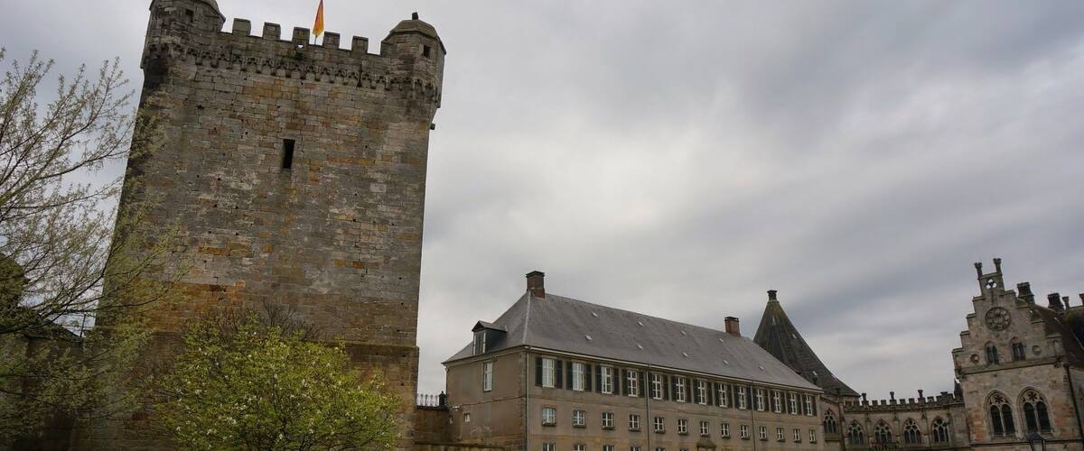 A historic castle with a tall tower, a large building with multiple windows, and a smaller tower with a clock.