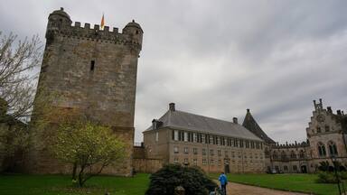 Un castillo histórico con una torre alta, un edificio grande con múltiples ventanas y una torre más pequeña con un reloj.
