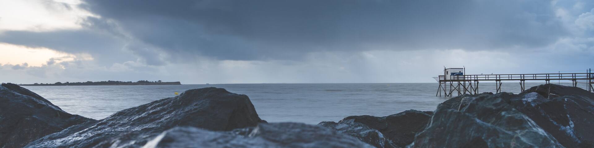 Typical old wooden fishing huts on stilts called « carrelet » in the atlantic ocean near La Rochelle, France. shot taken at sunset on a stormy day.