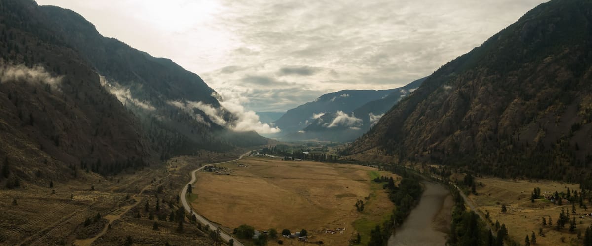 A valley with a river, surrounded by mountains and a cloudy sky.
