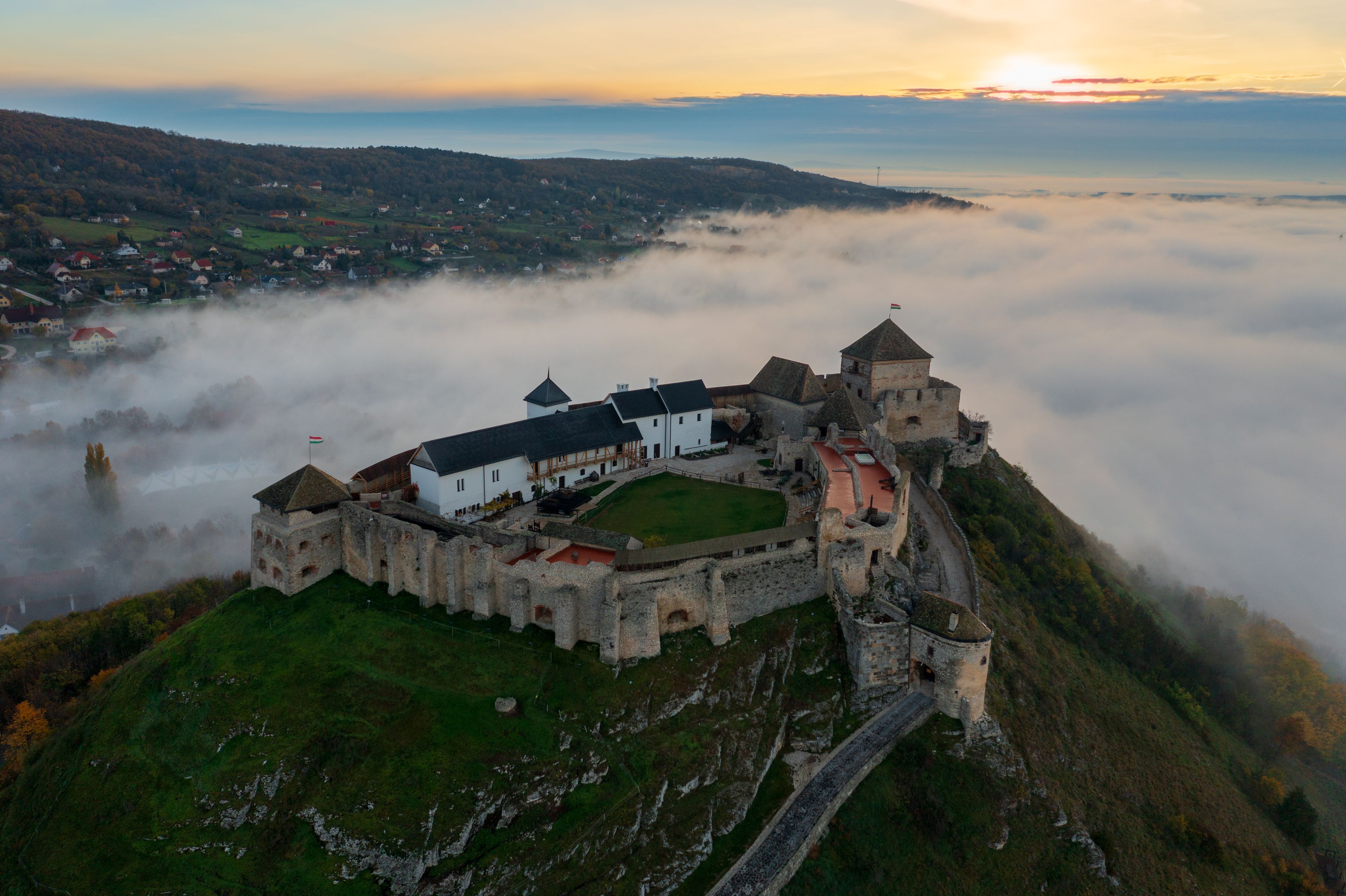 A castle perched atop a hill, surrounded by mist and overlooking a valley.