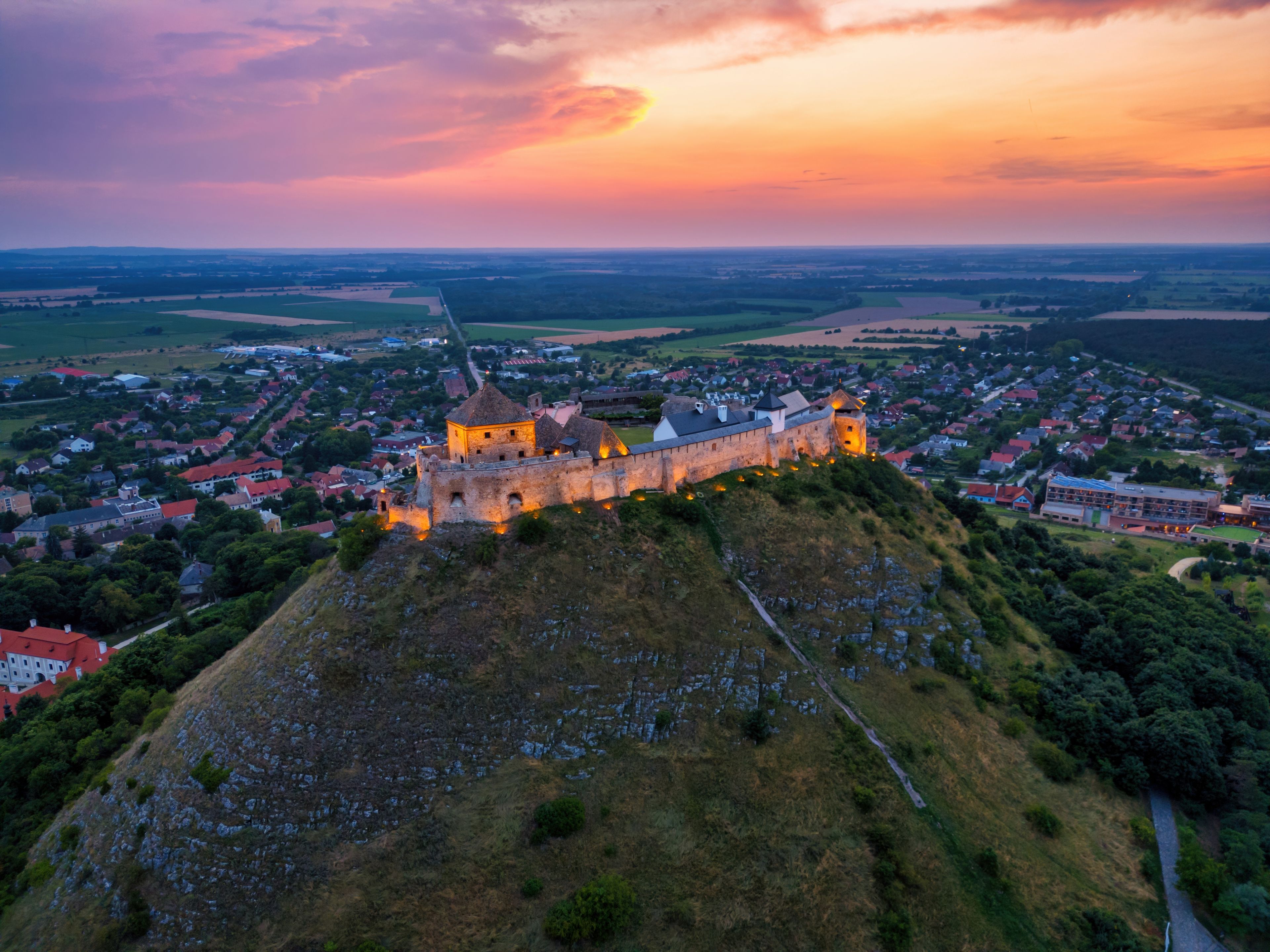 A historic castle on a hill overlooking a town at sunset.