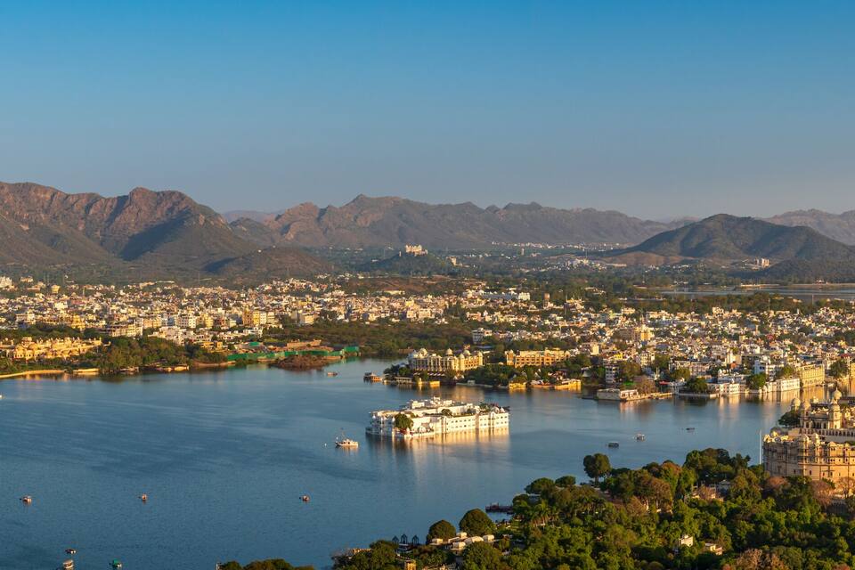 Un paysage urbain avec une vaste étendue d’eau, des montagnes en arrière-plan et un imposant édifice qui ressemble à un château.