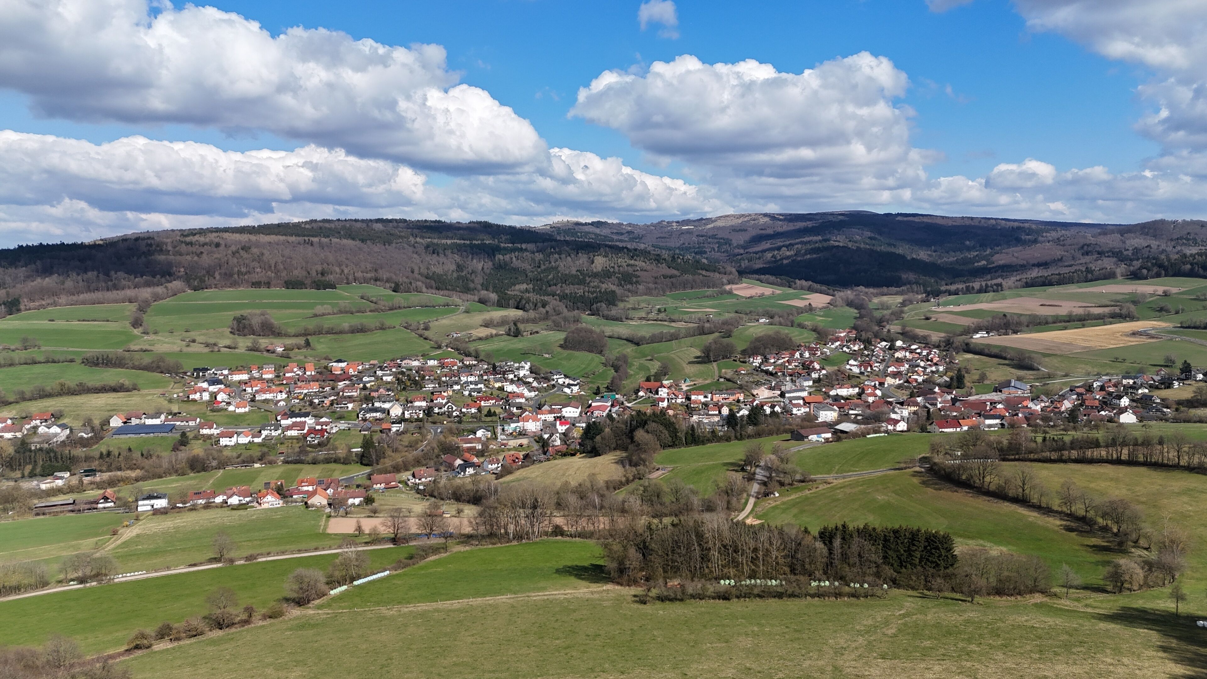 A rural town nestled in rolling hills with green fields and scattered houses.