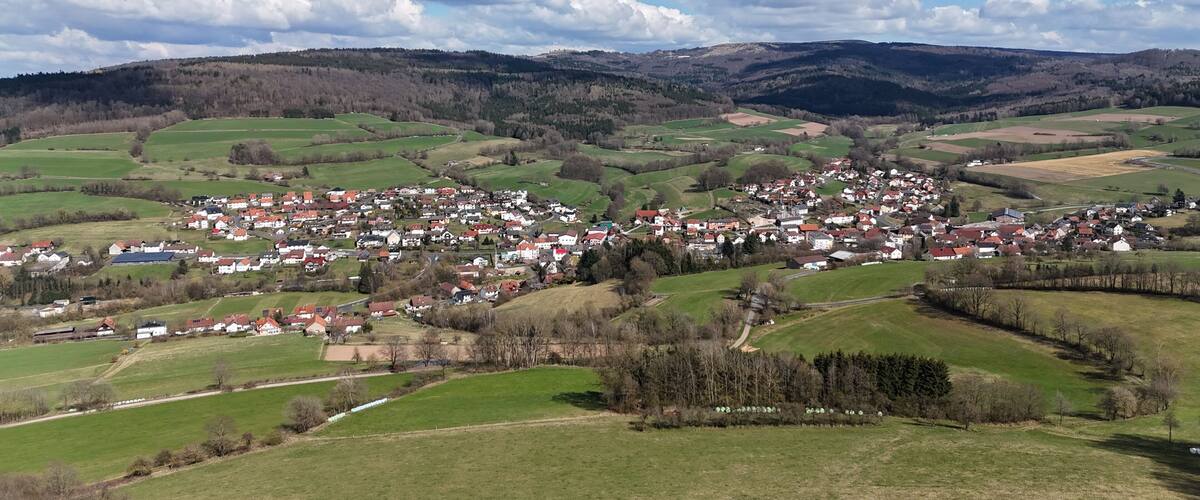 A rural town nestled in rolling hills with green fields and scattered houses.