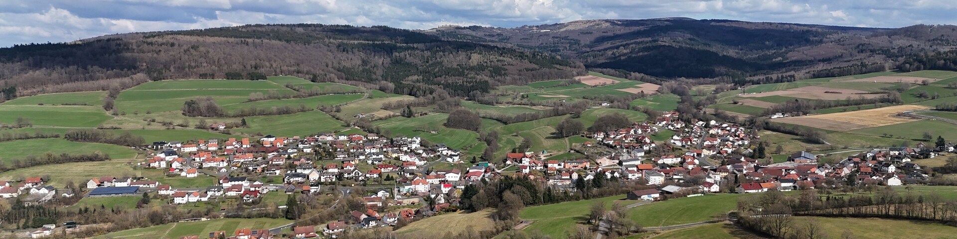 A rural town nestled in rolling hills with green fields and scattered houses.