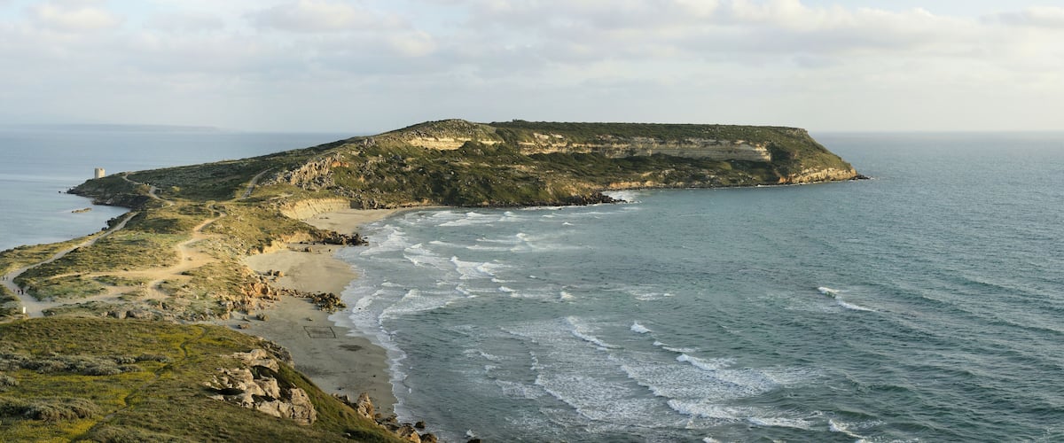 Un paysage côtier avec une plage de sable, des falaises rocheuses et un sentier sinueux.