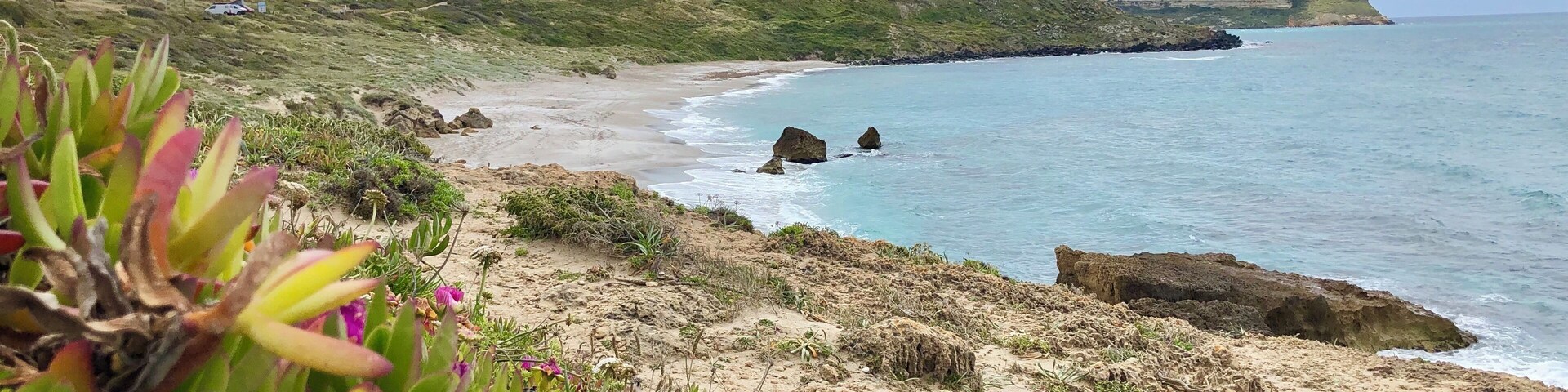 A coastal landscape with a hilltop castle, sandy beach, and rocky shoreline.