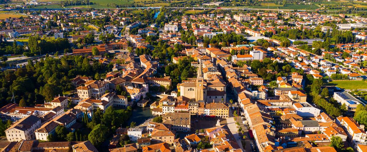 An aerial view of a historic town with a prominent church, dense residential areas, and surrounding green fields.