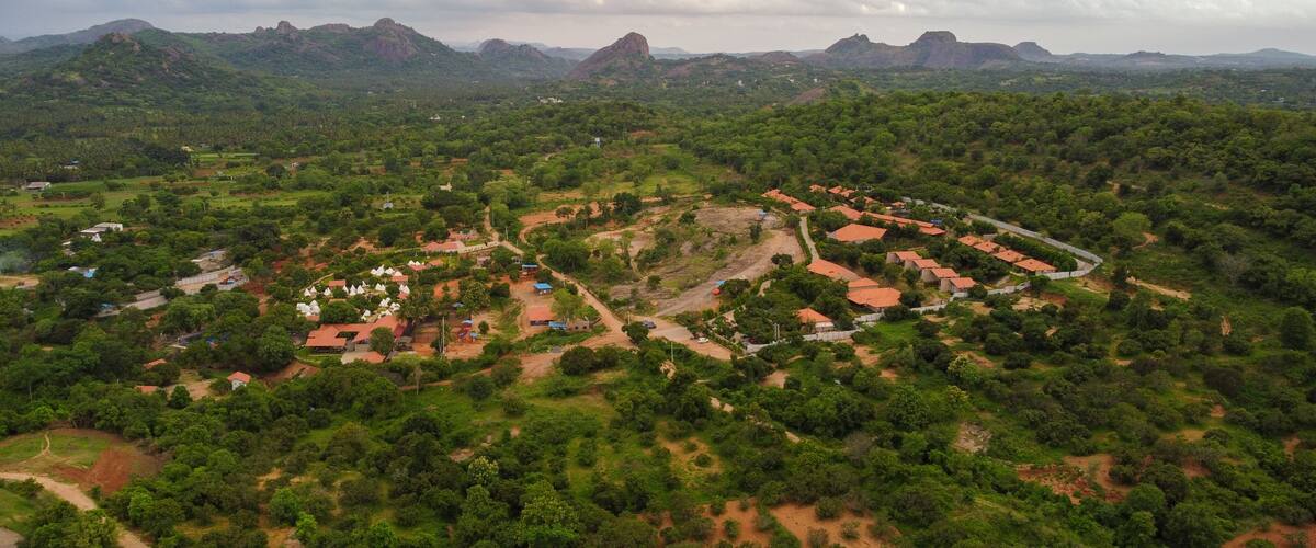 A rural landscape with a cluster of houses surrounded by dense greenery and hills in the background.