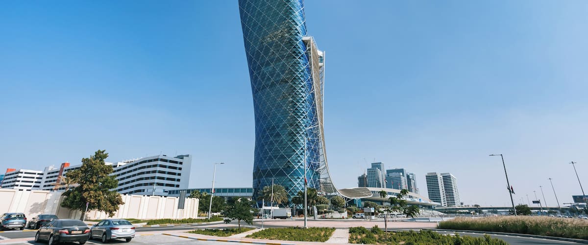 Un edificio alto y de forma peculiar con fachada de vidrio azul, rodeado por un paisaje urbano con arquitectura moderna.