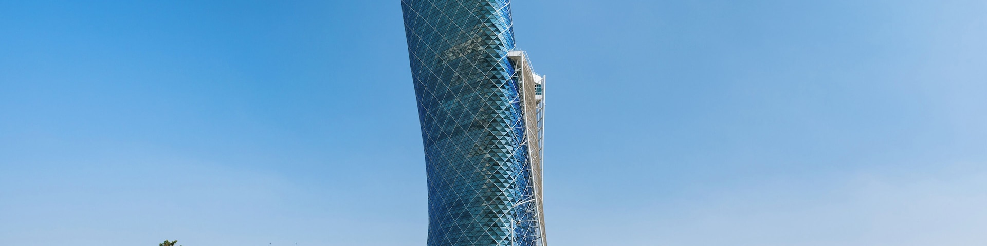 A tall, uniquely shaped building with a blue glass facade, surrounded by a cityscape with modern architecture.