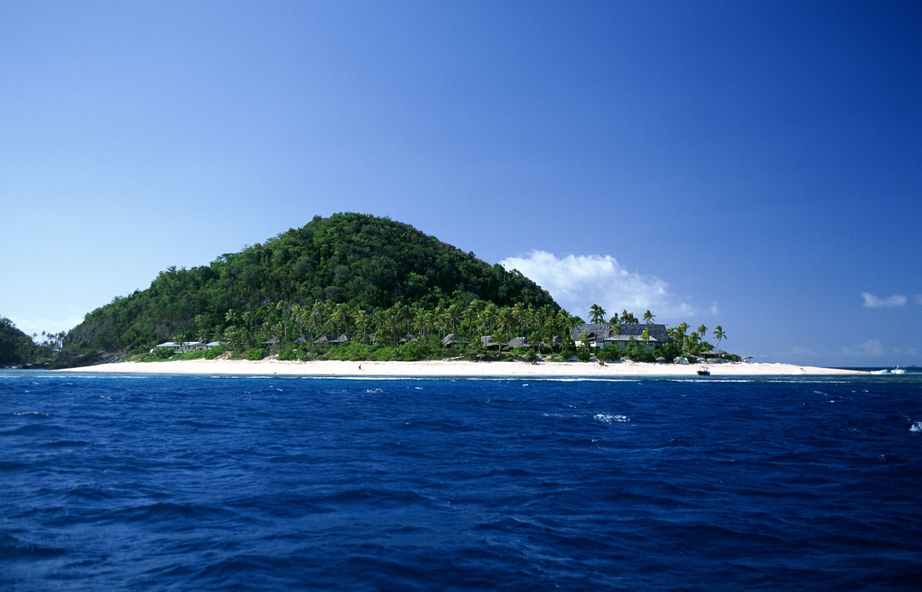 A tropical island with a beach and dense forest.