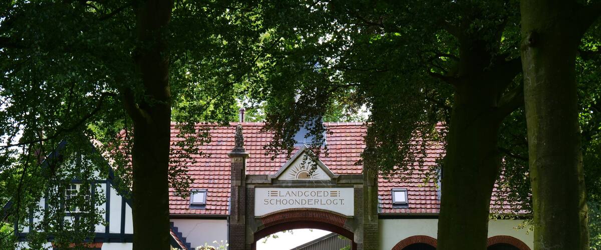 A pathway leading to a building with a red-tiled roof and a sign reading "Landgoed Schoonderlog I."