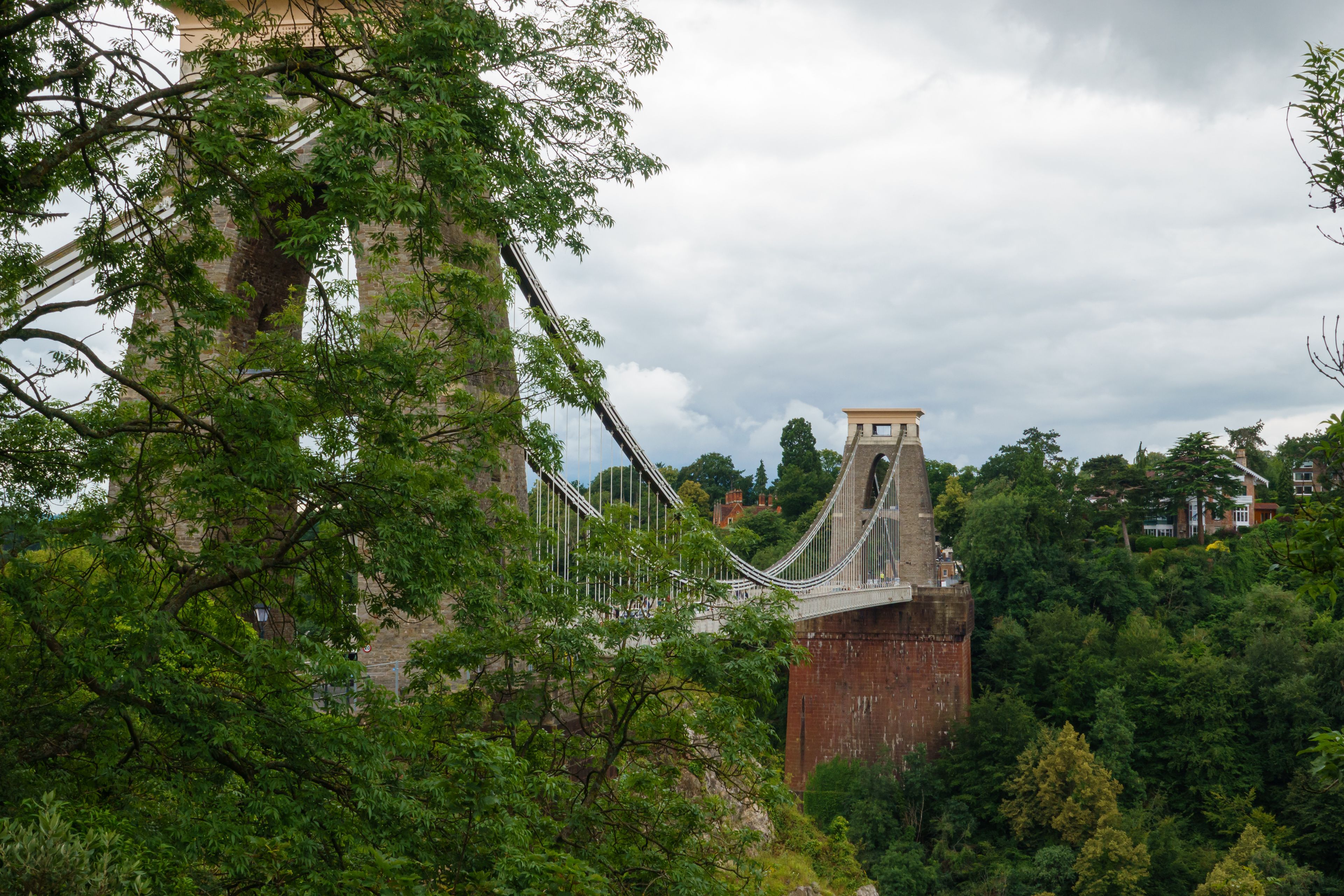 A suspension bridge with a brick tower, surrounded by dense green foliage.