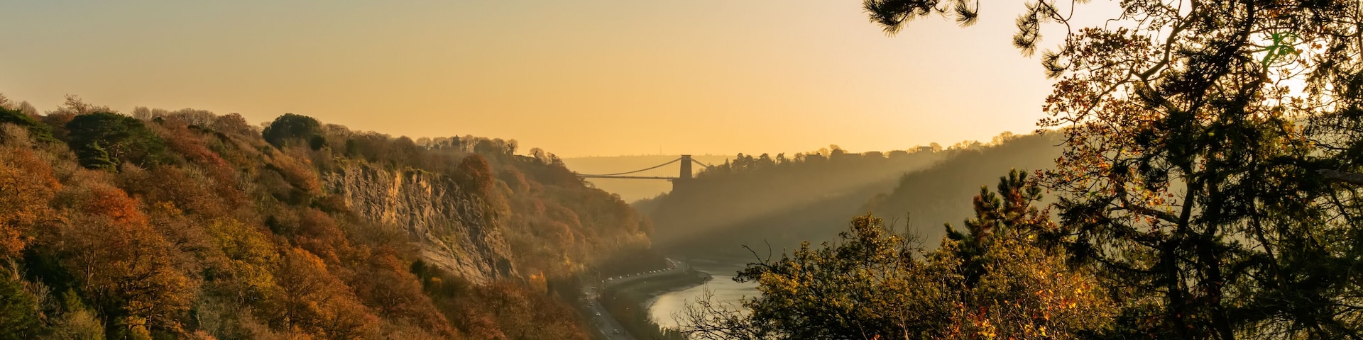 A river valley with autumn foliage, a bridge, and a mountainous backdrop.