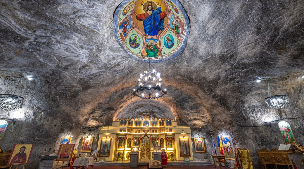 An interior of a cave church with a large circular icon above the altar, stone walls, and a chandelier.