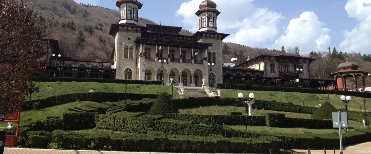 A historic building with two towers, surrounded by well-manicured gardens and hills.