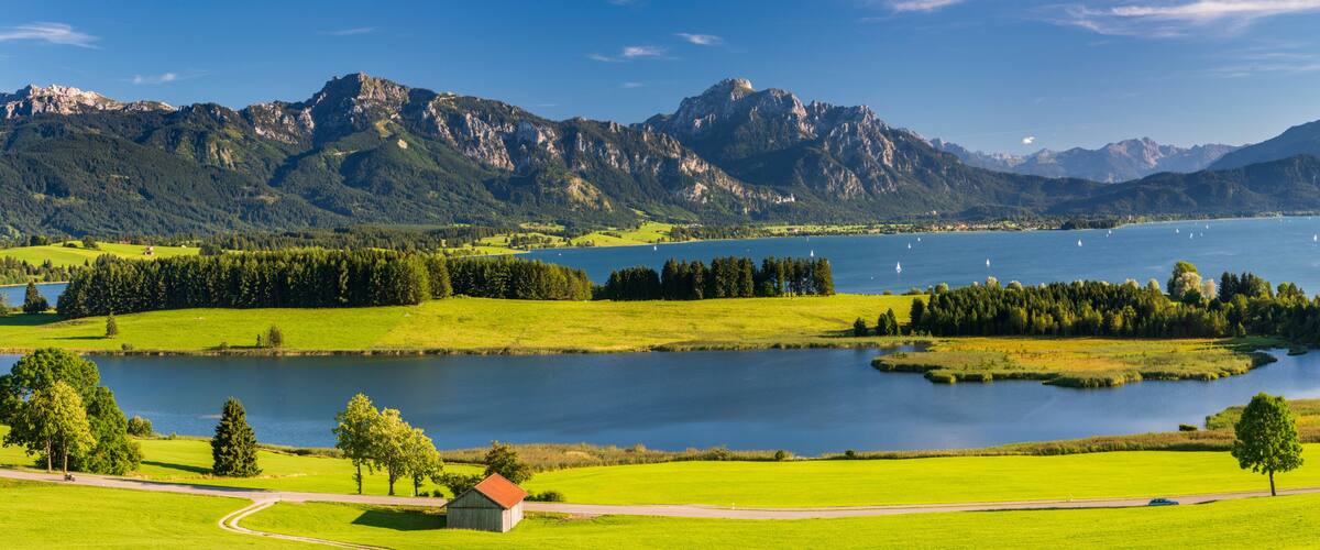 A lake surrounded by mountains, a small wooden house, and a clear blue sky.