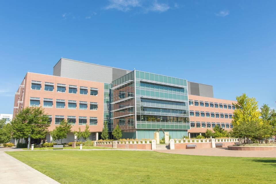 A modern building with multiple floors, large windows, and a green glass facade.