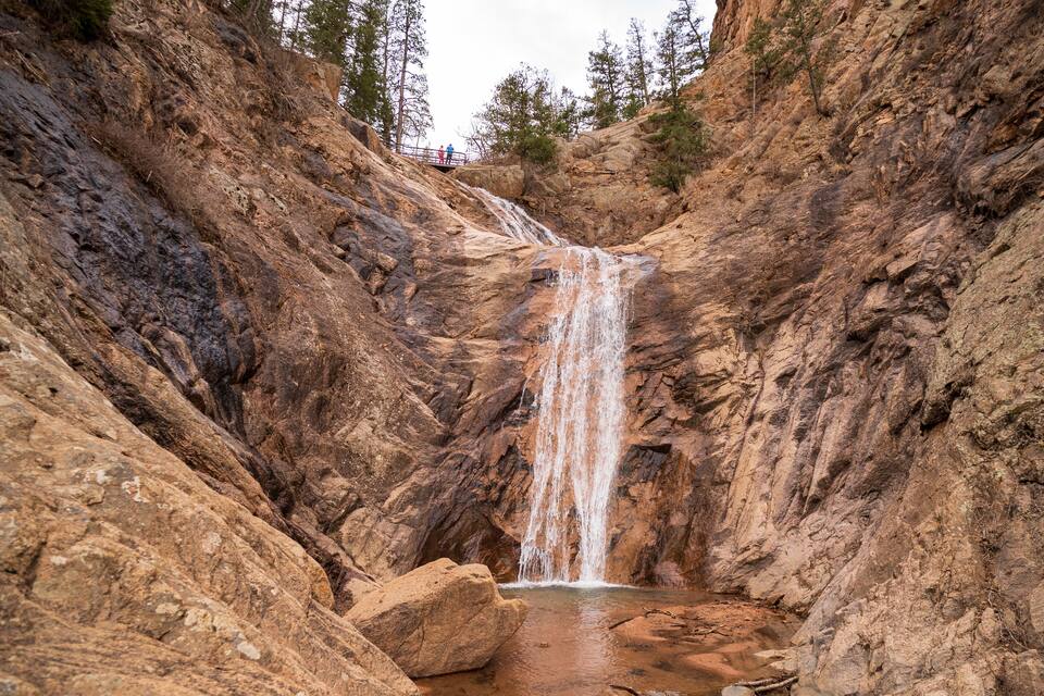 Ein Wasserfall stürzt durch eine felsige Schlucht, umgeben von Bäumen.
