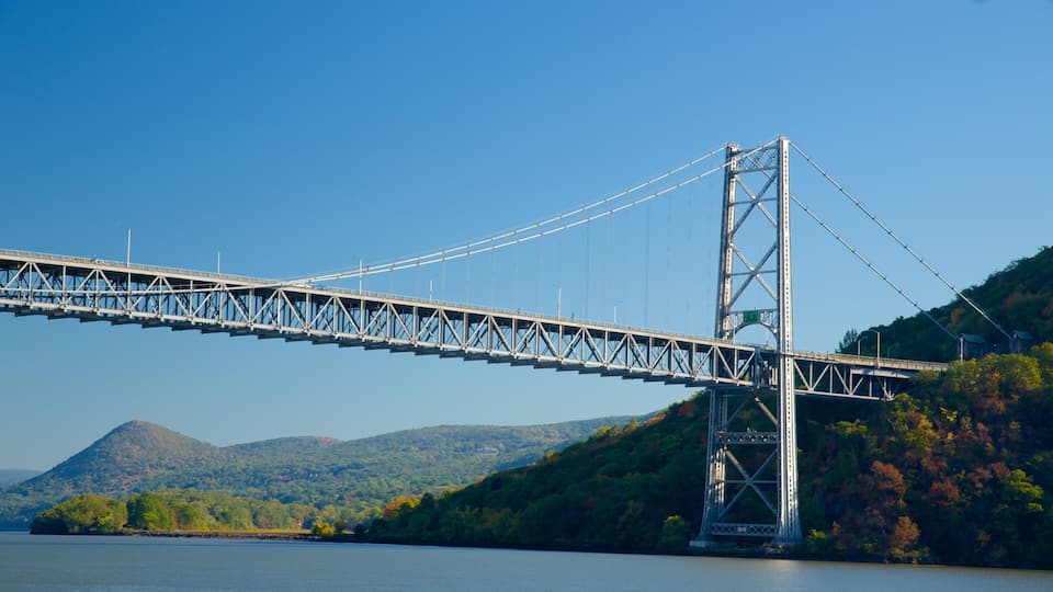 A large suspension bridge spanning a river, surrounded by hills and autumn foliage.