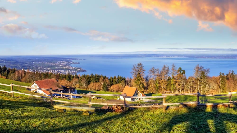 A panoramic view of a coastal landscape with a wooden fence, houses, and a distant body of water.