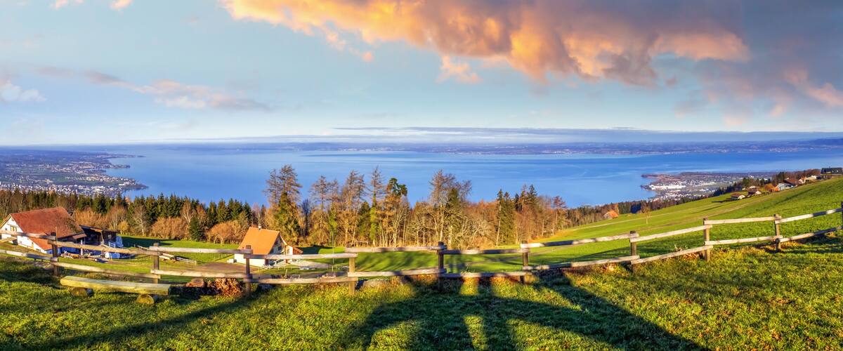 A panoramic view of a coastal landscape with a wooden fence, houses, and a distant body of water.