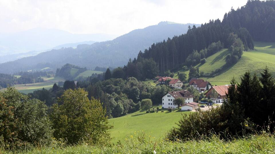 A rural landscape with rolling hills, a village with red-roofed houses, and dense forested areas.