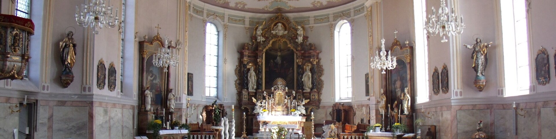 An ornate church interior with pews, chandeliers, and religious statues.