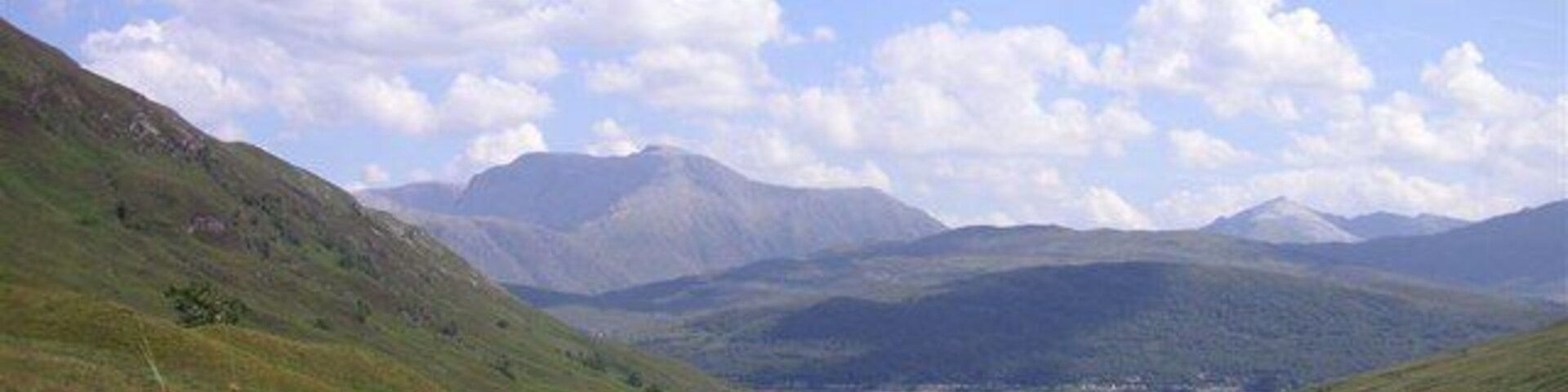 Un valle con colinas ondulantes, cielo despejado y montañas a lo lejos.