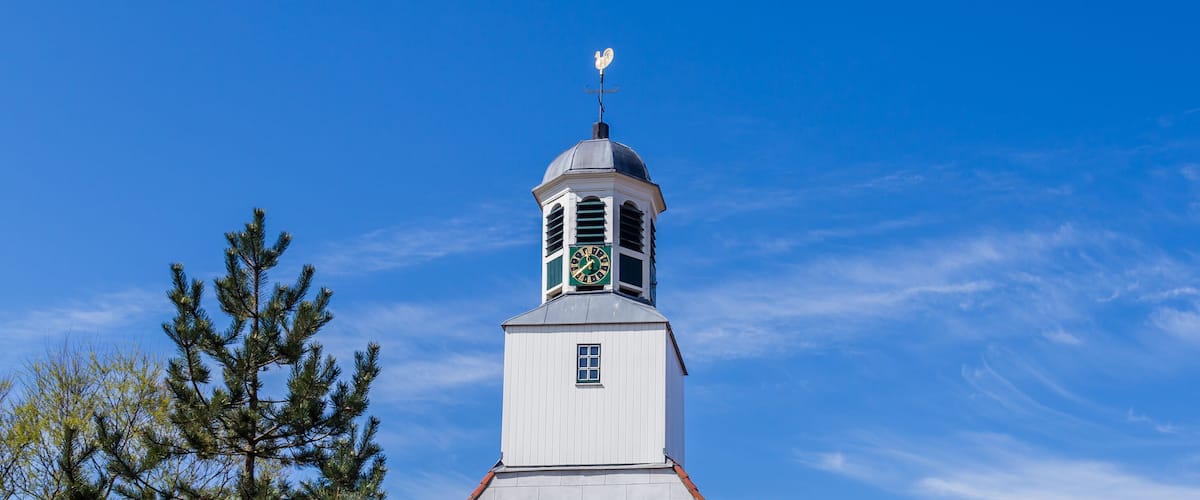 A white clock tower with a weather vane on top, set against a clear blue sky.