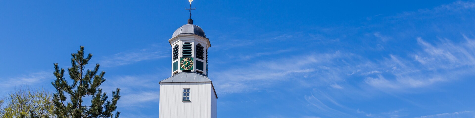 A white clock tower with a weather vane on top, set against a clear blue sky.