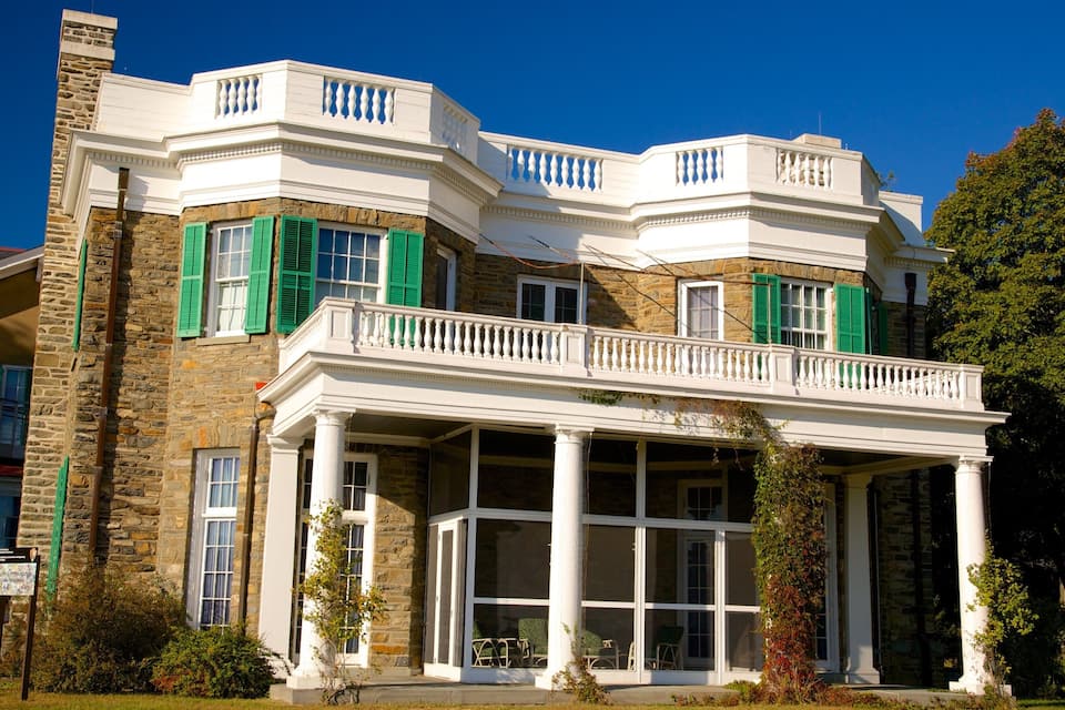 A large, historic house with a stone facade, green shutters, and a covered porch.