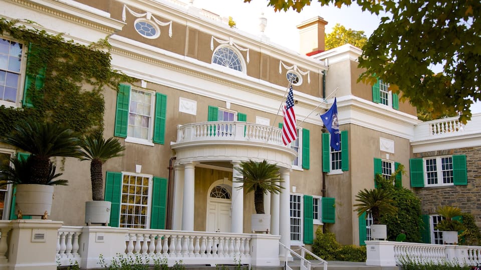 A stately building with green shutters, an American flag, and a blue flag.