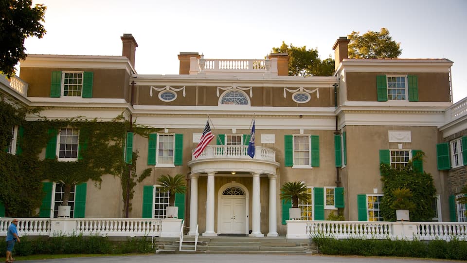A large, historic building with green shutters, a central entrance with columns, and two flags.
