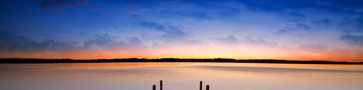 A wooden pier extending into calm water with a sunset sky.